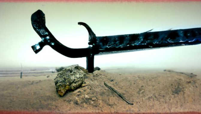 Ein korrodiertes Schwert im Sand.