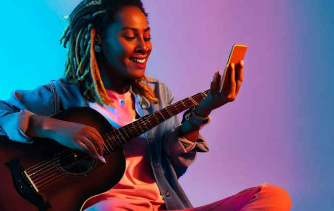 Frau mit einer Gitarre hält ein Smartphone in der Hand.